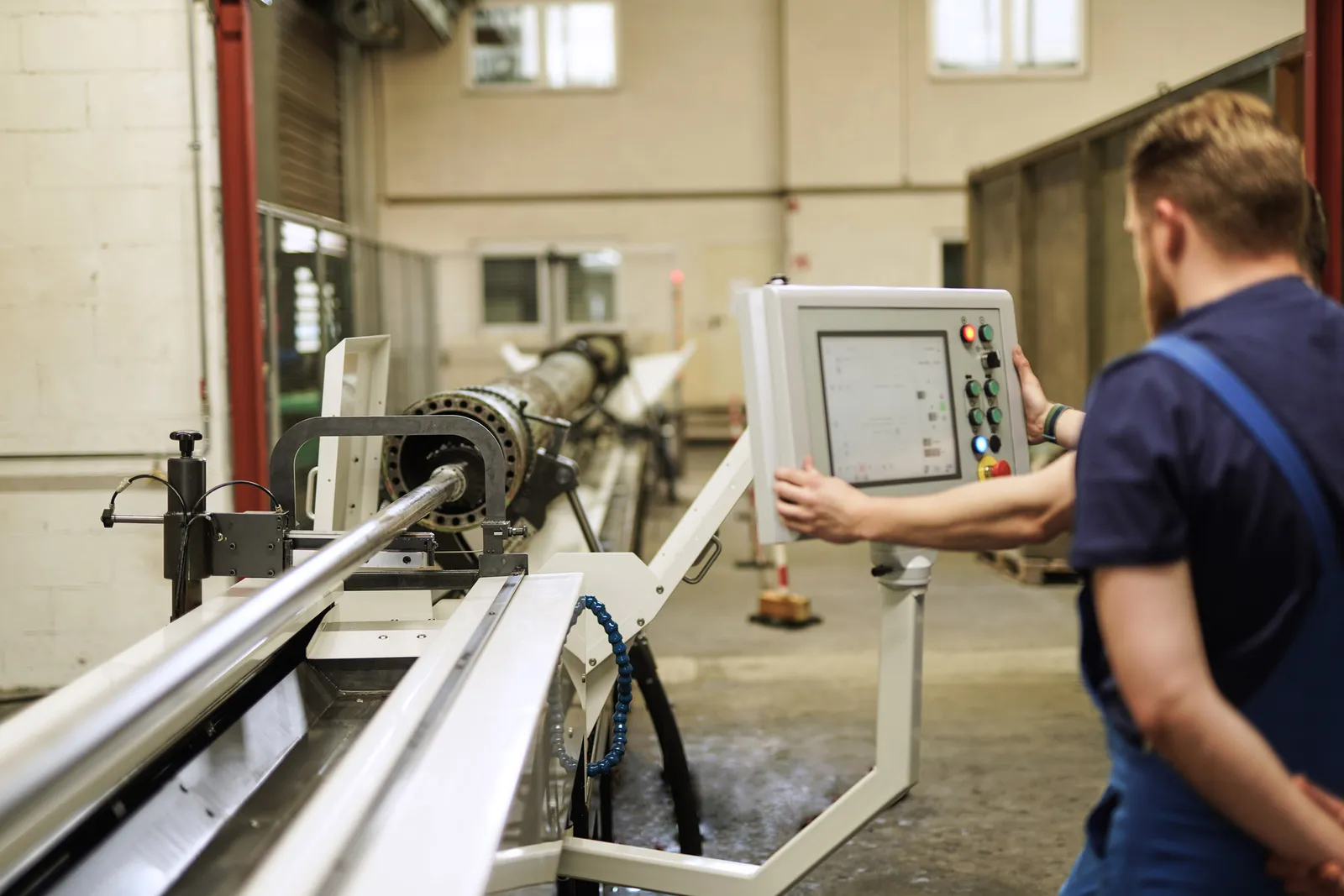 Mitarbeiter bedient die Steuerung einer langen Bearbeitungsmaschine für Zylinderrohre