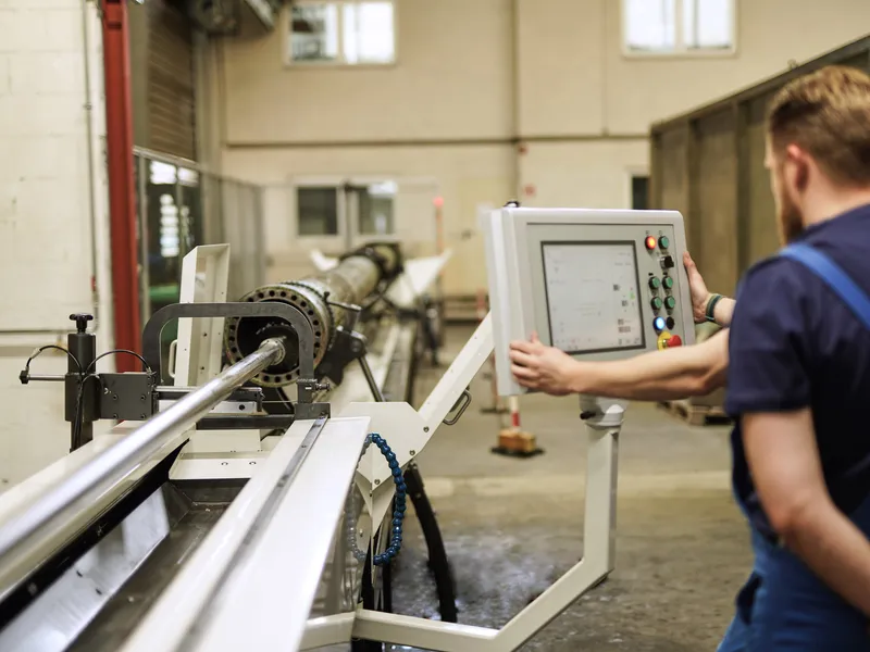 Mitarbeiter bedient die Steuerung einer langen Bearbeitungsmaschine für Zylinderrohre