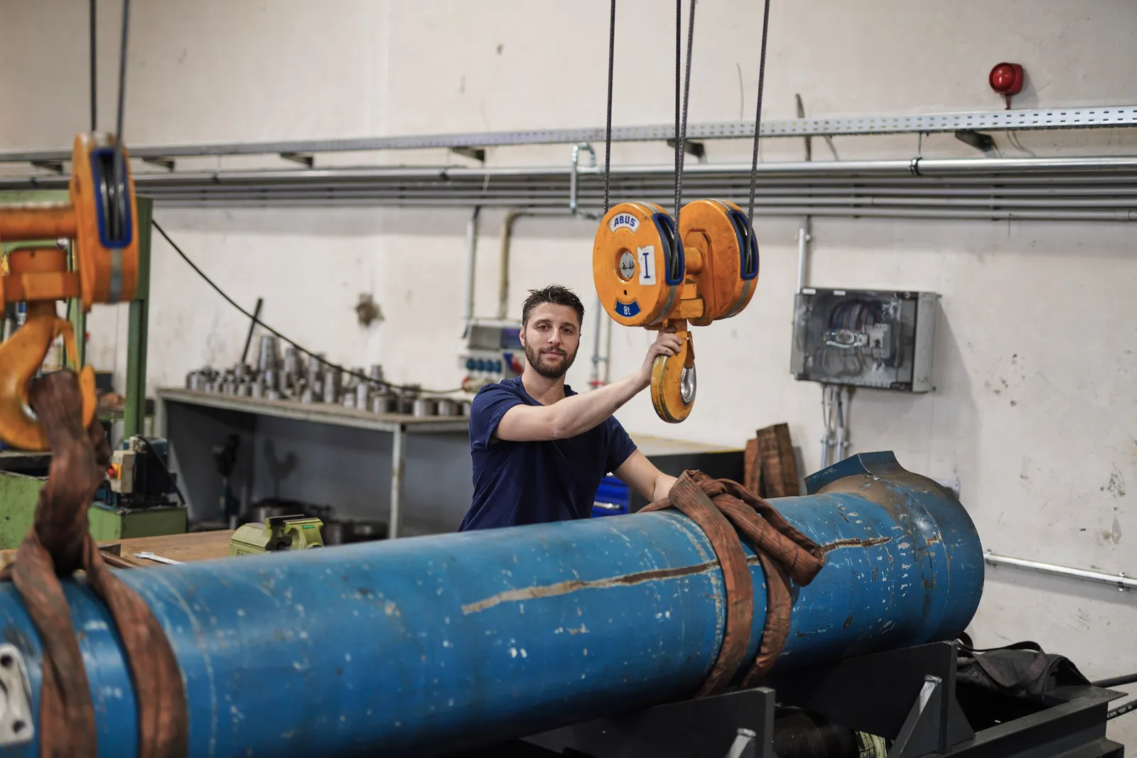Mitarbeiter führt einen großen Hydraulikzylinder am Hallenkran