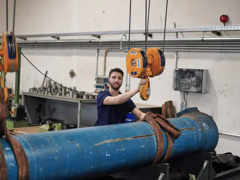 Mitarbeiter führt einen großen Hydraulikzylinder am Hallenkran