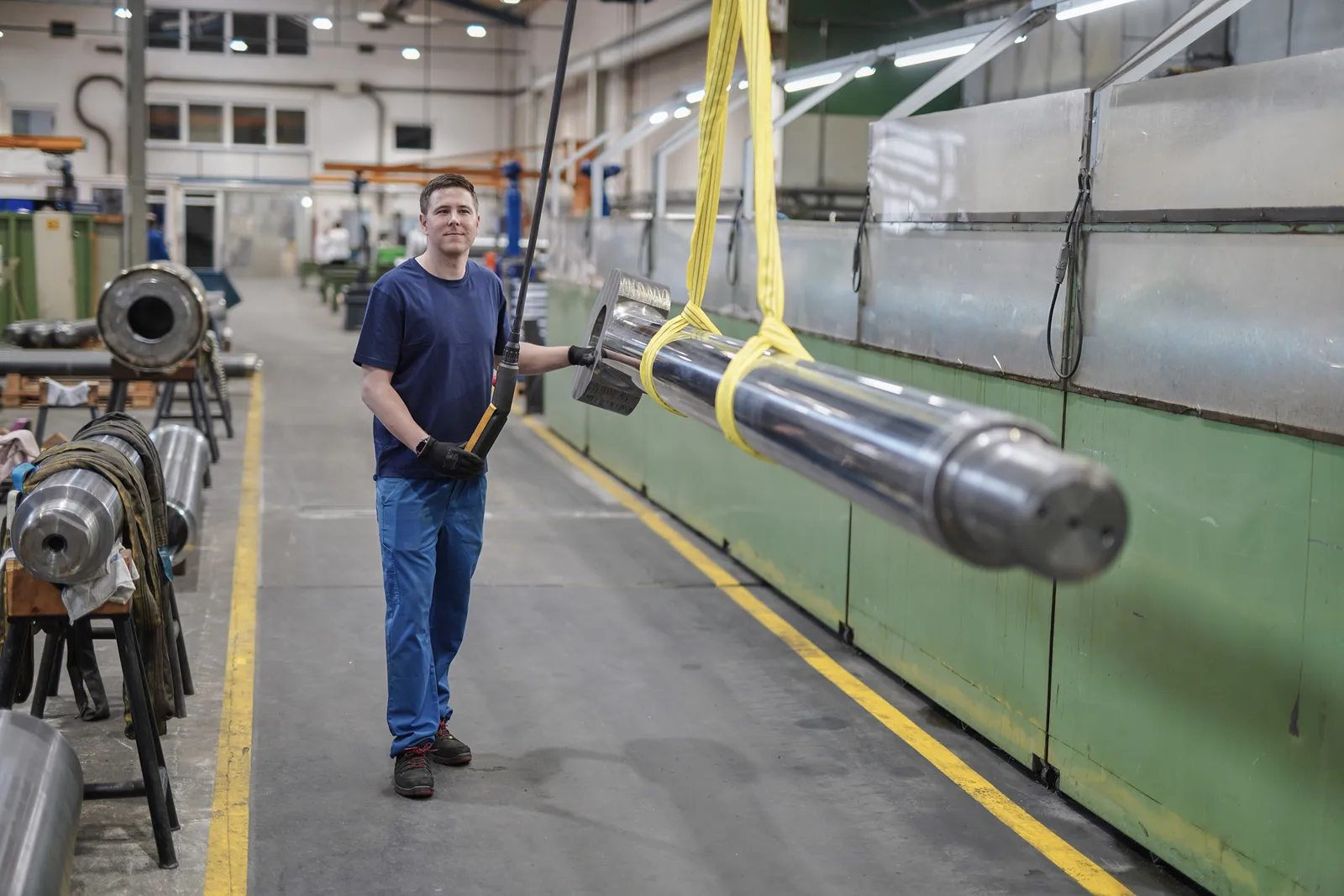 Mitarbeiter transportiert eine Kolbenstange mit dem Hallenkran durch die Werkhalle