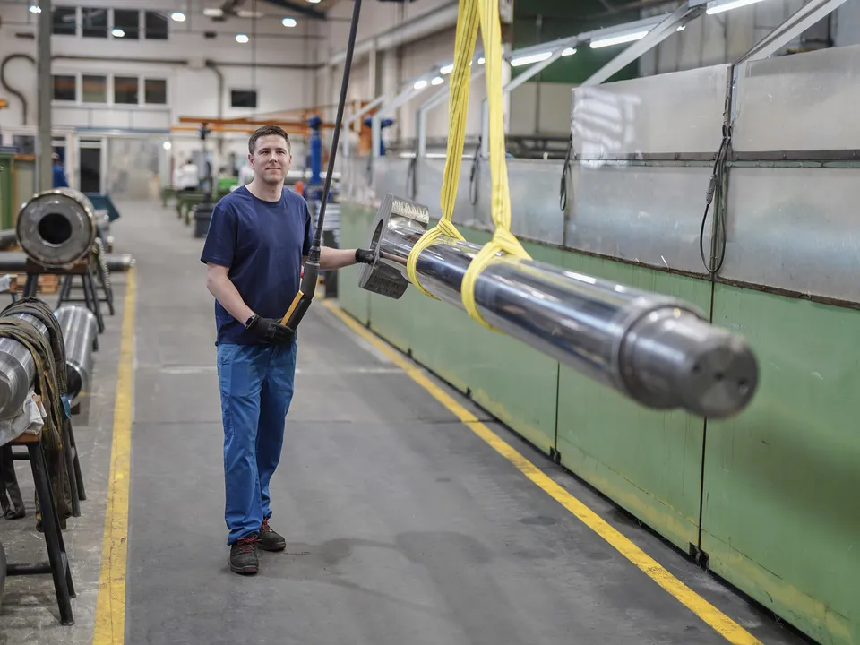 Mitarbeiter transportiert eine Kolbenstange mit dem Hallenkran durch die Werkhalle