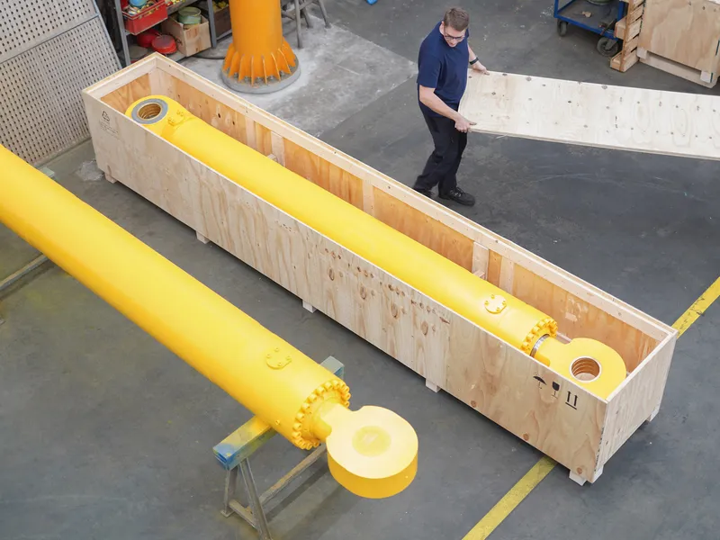 Mitarbeiter neben einem gelben Hydraulikzylinder in der Holz-Transportkiste