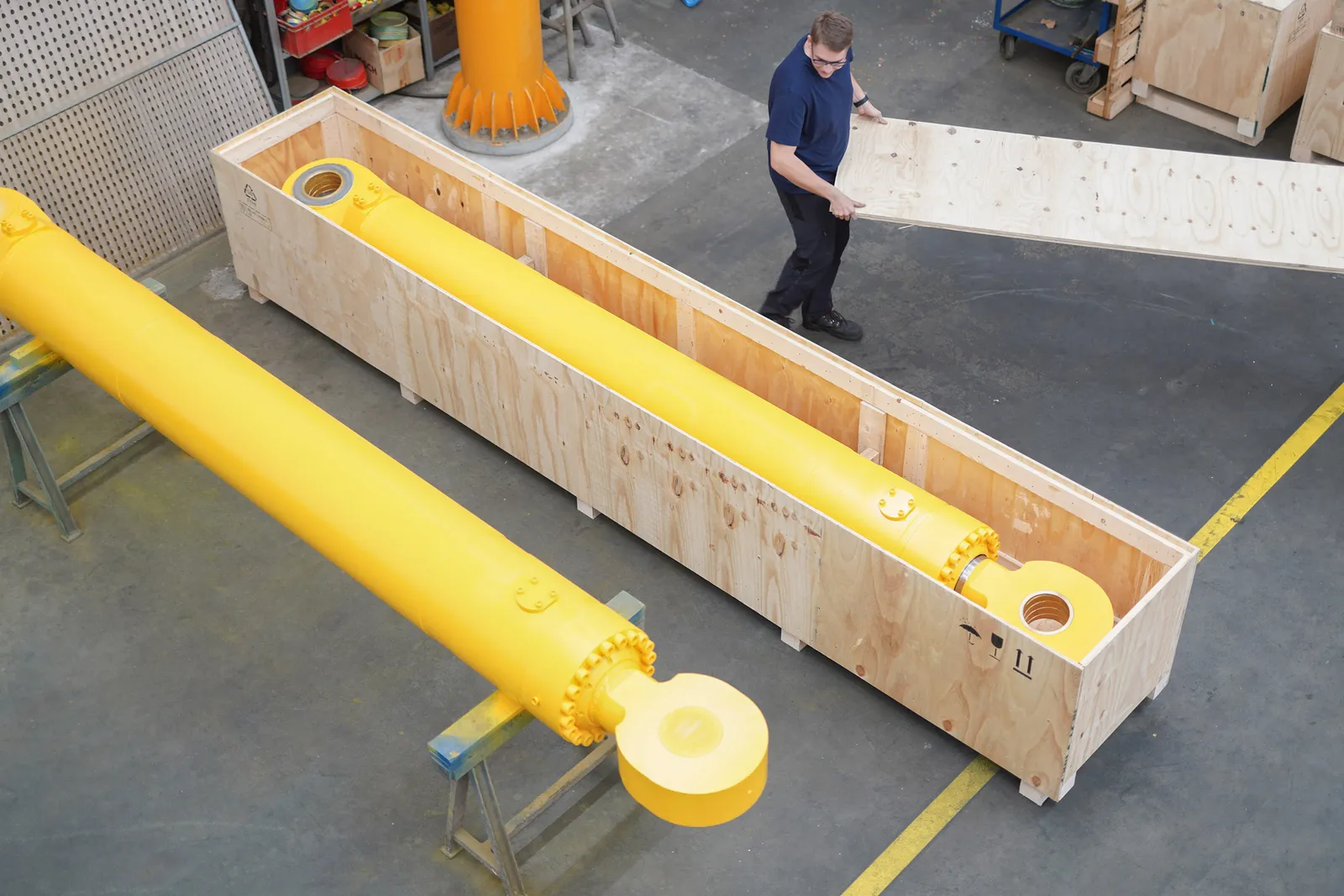 Mitarbeiter neben einem gelben Hydraulikzylinder in der Holz-Transportkiste