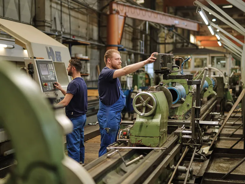 Zwei Mitarbeiter richten gemeinsam eine konventionelle Drehmaschine ein