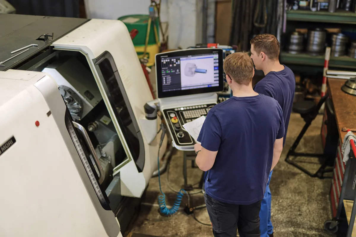Zwei Mitarbeiter prüfen ein CAD-Programm am Bildschirm einer CNC-Maschine