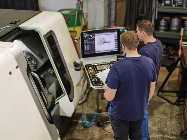 Zwei Mitarbeiter prüfen ein CAD-Programm am Bildschirm einer CNC-Maschine