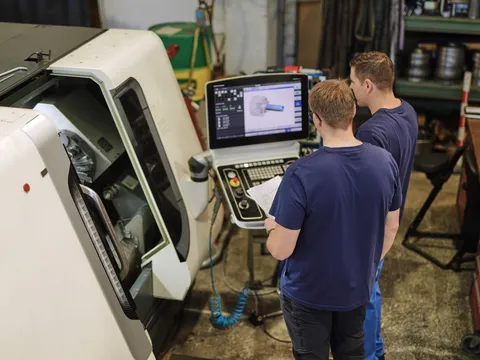 Zwei Mitarbeiter prüfen ein CAD-Programm am Bildschirm einer CNC-Maschine