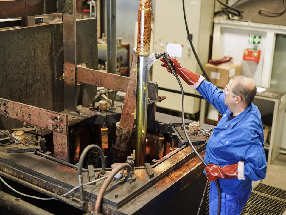 Mitarbeiter mit Schutzhandschuhen und Schutzbrille hebt ein Bauteil aus dem Chrombad