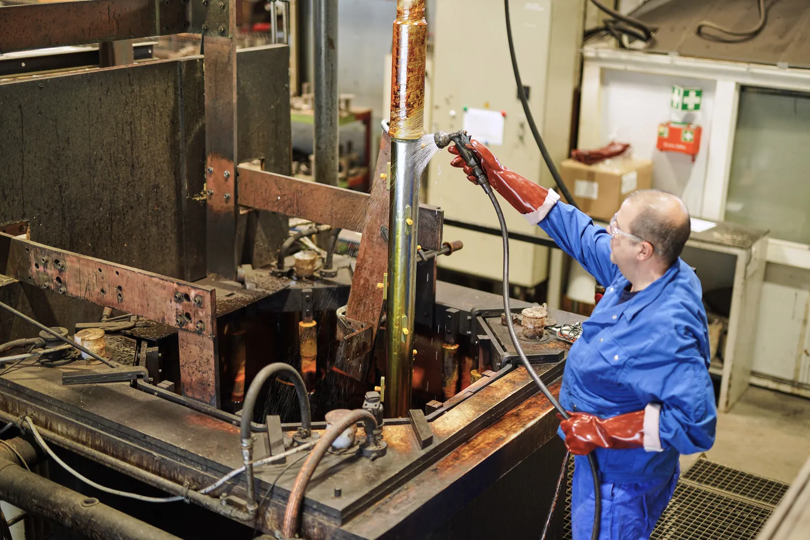 Mitarbeiter mit Schutzhandschuhen und Schutzbrille hebt ein Bauteil aus dem Chrombad