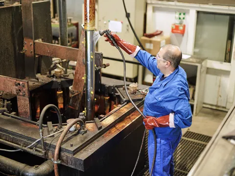 Mitarbeiter hängt ein Bauteil in das Chrombad der eigenen Hartverchromung