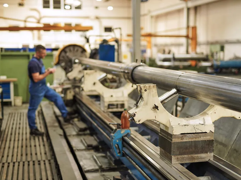 Mitarbeiter bearbeitet eine mehrere Meter lange Kolbenstange auf der Drehmaschine