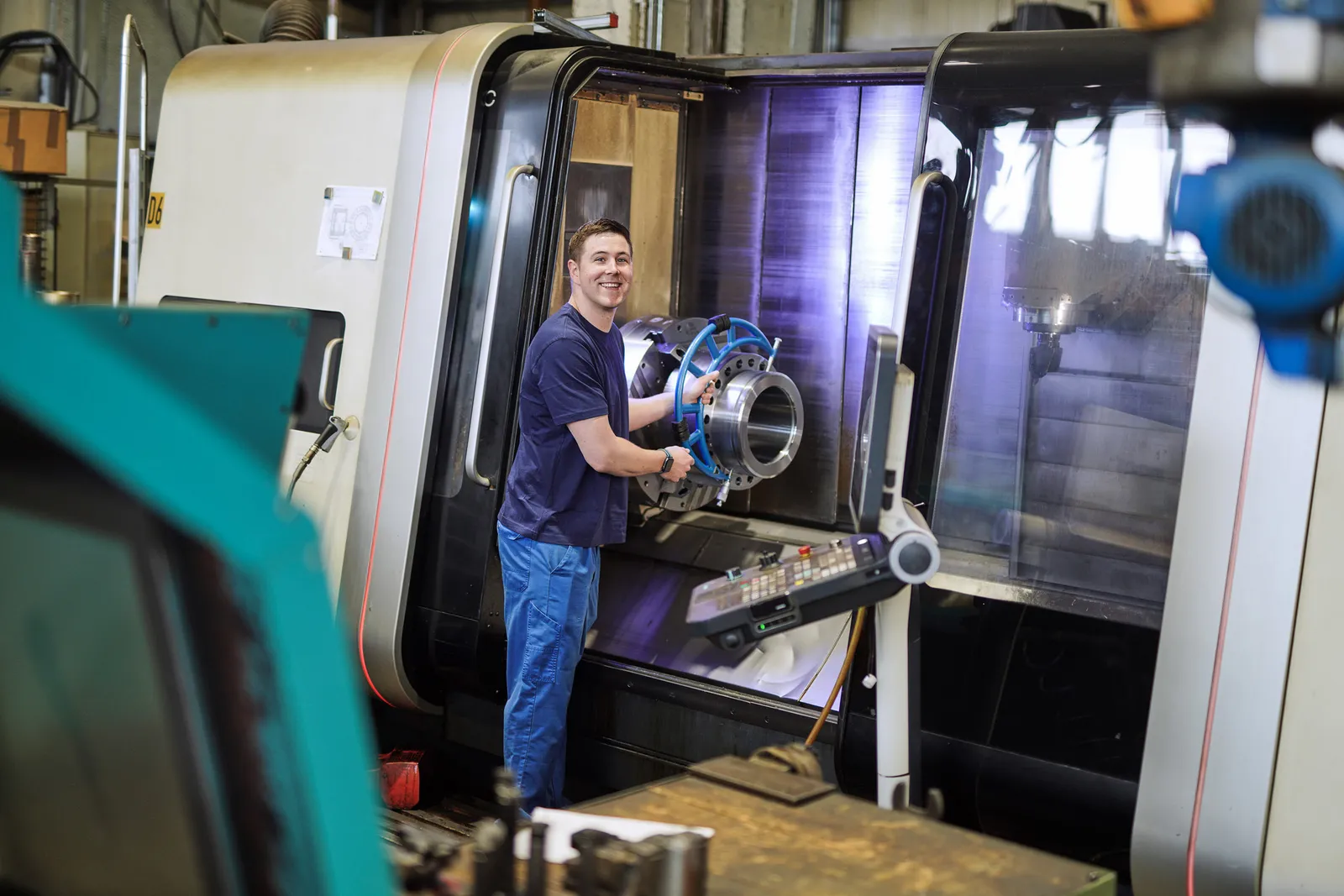 Mitarbeiter öffnet die Tür einer CNC-Maschine und hält ein gedrehtes Bauteil