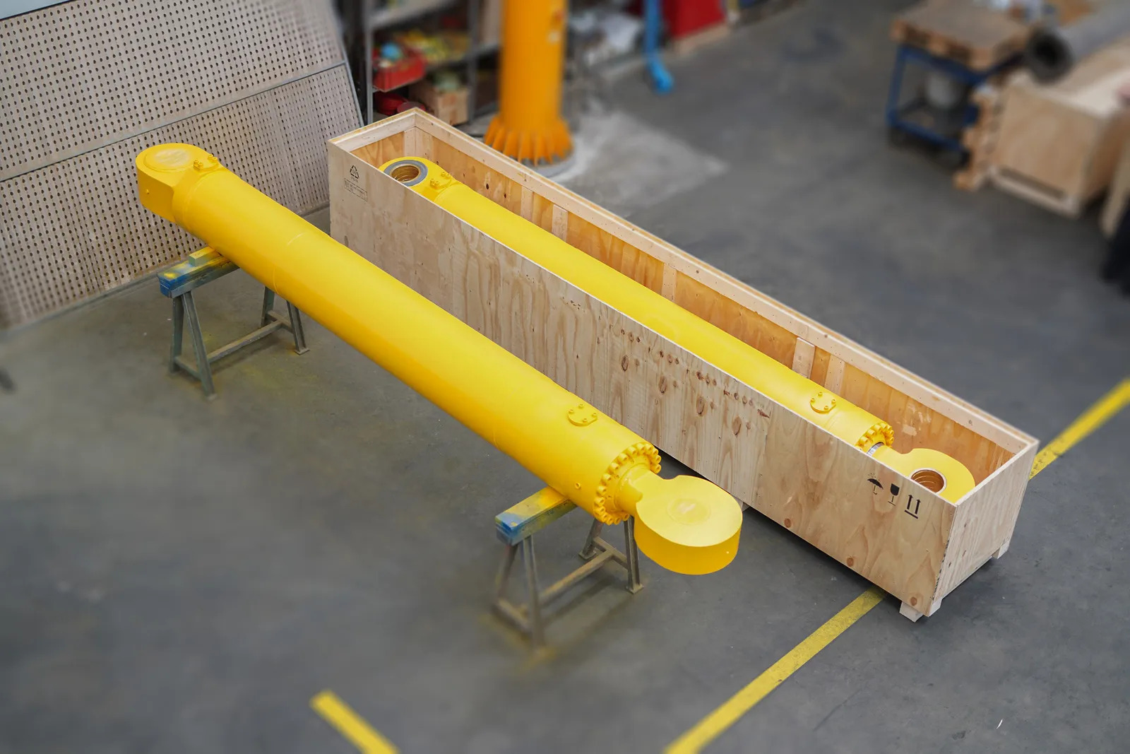 Frisch lackierter gelber Hydraulikzylinder in einer Holz-Transportkiste in der Werkhalle