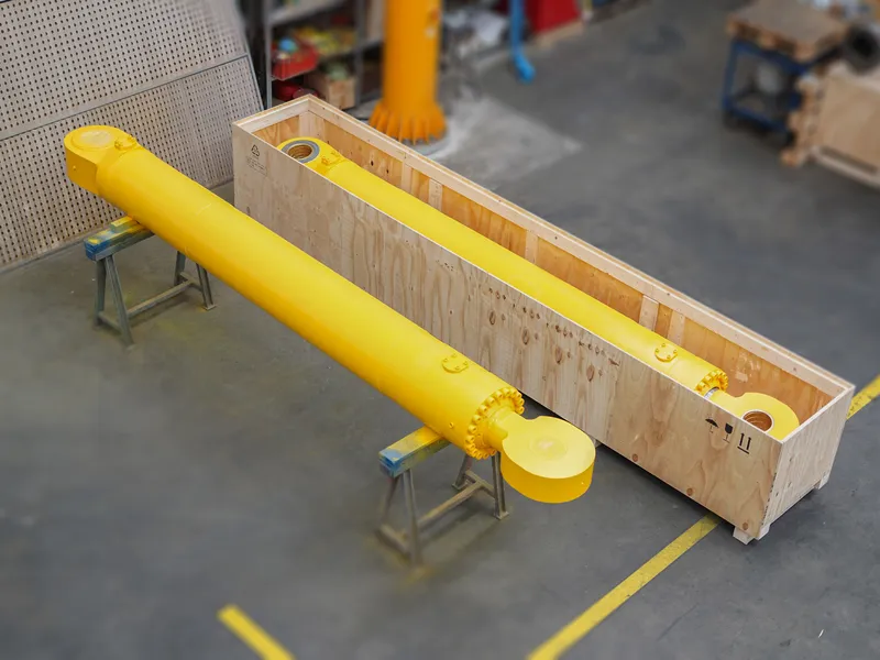 Frisch lackierter gelber Hydraulikzylinder in einer Holz-Transportkiste in der Werkhalle