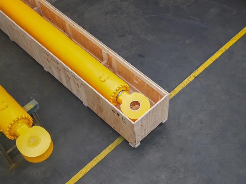 Gelber Hydraulikzylinder, fertig verpackt in einer Holzkiste, auf dem Hallenboden mit gelber Markierung