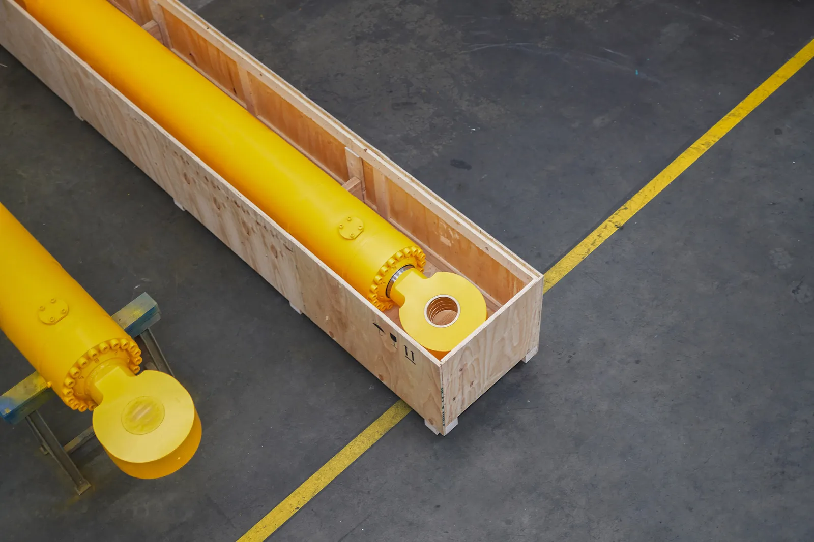 Gelber Hydraulikzylinder, fertig verpackt in einer Holzkiste, auf dem Hallenboden mit gelber Markierung